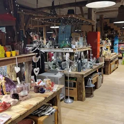 Winkelvloer met houten display-tafels vol huishoudartikelen, decoratie en diversen, onder sfeervolle verlichting
