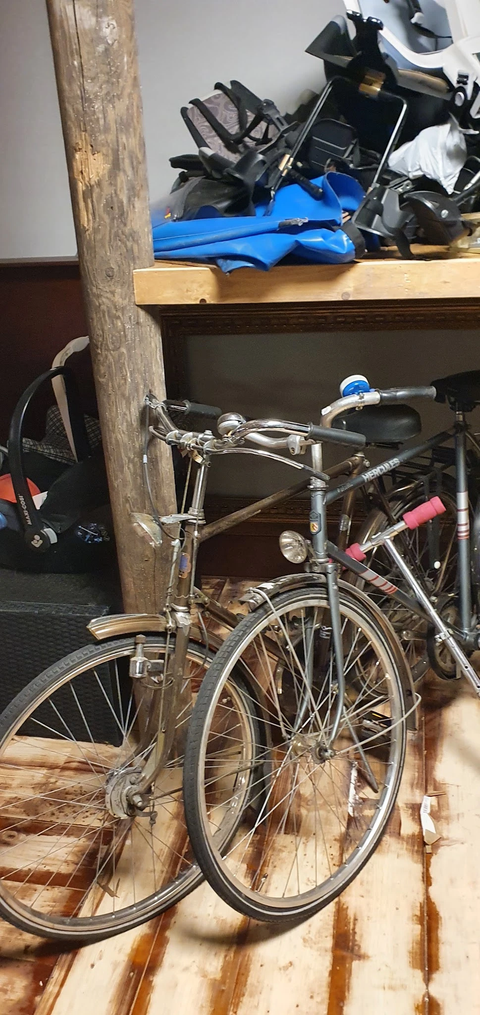 Tweedehands fiets tegen een houten paal, met blauwe versnellingshevel en rode zadel