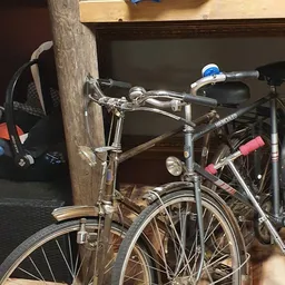 Tweedehands fiets tegen een houten paal, met blauwe versnellingshevel en rode zadel
