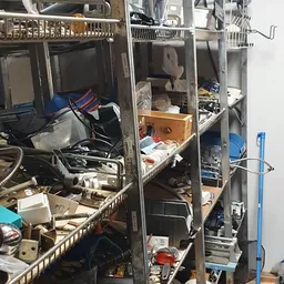 Overvol rek in kringloopwinkel met diverse gebruikte spullen, dozen en huishoudartikelen