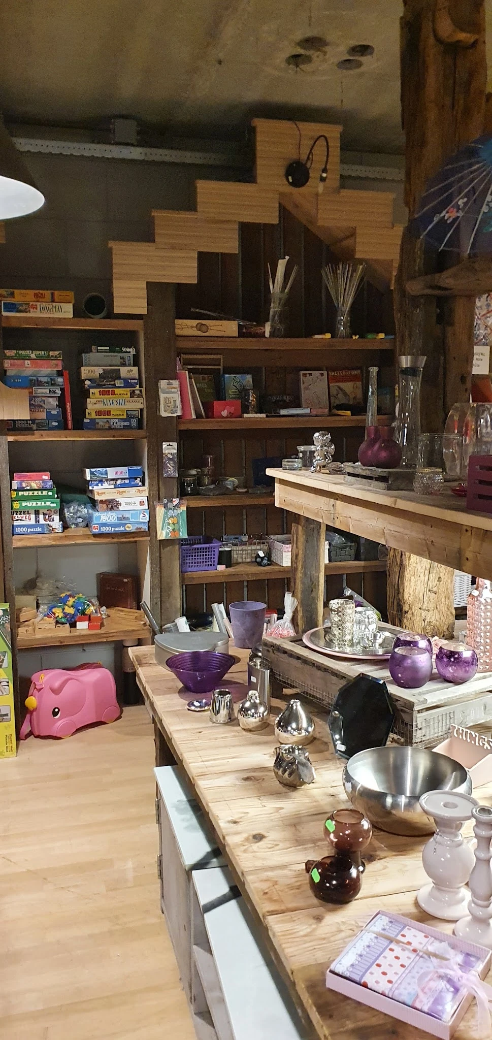 Houten stellingkast met diverse tweedehands huisartikelen: bordspellen, boeken, paarse serviesgoed, kristallen ornamentjes en