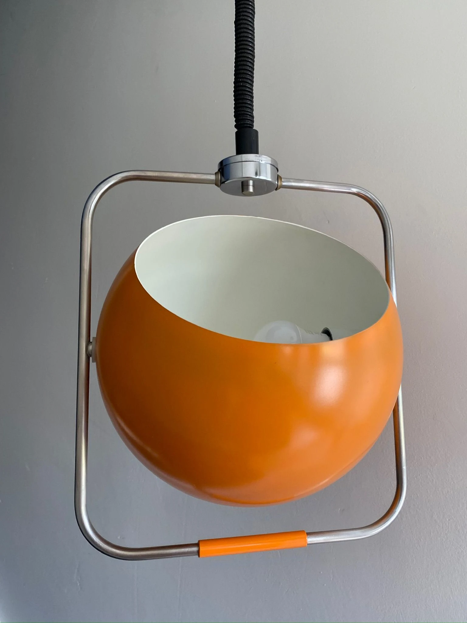 Oranje hanglamp met wit binnenwerk en chromen beugel tegen grijze achtergrond