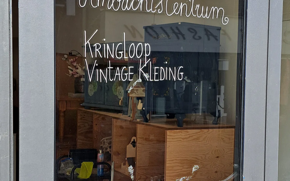 Etalageruit met witte handgeschreven teksten over vintage kleding en interieur