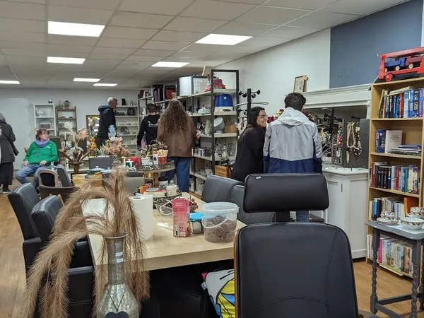 Winkelvloer met tafels, stellingen met boeken en spullen, bezoekers in de kringloopwinkel