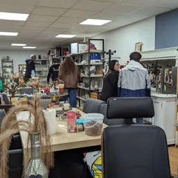 Winkelvloer met tafels, stellingen met boeken en spullen, bezoekers in de kringloopwinkel