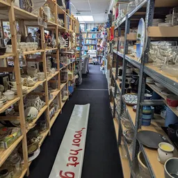 Winkelpad tussen houten stellingen vol gebruiksartikelen, boeken en servies in een kringloopwinkel