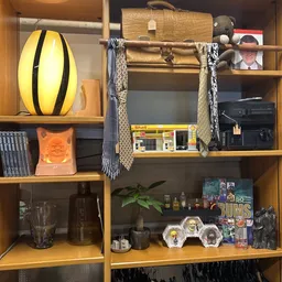 Houten wandkasten met diverse spullen: gele lamp, boeken, oranje object, glazen, planten, decoraties en spiegellijst