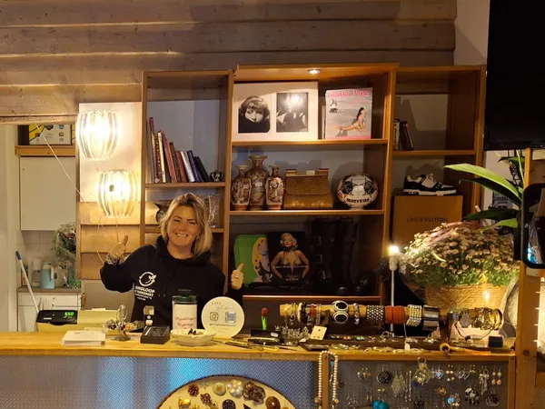 Winkelinterieur met houten wandkasten, uitgestalde spullen, verlichting en een vrouw achter de toonbank