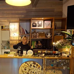 Winkelinterieur met houten wandkasten, uitgestalde spullen, verlichting en een vrouw achter de toonbank