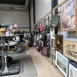 Winkelvloer met kledingrekken, kunstwerk aan muren en werktafel met artikelen