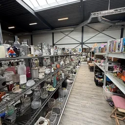 Stellingen vol verschillende huishoudartikelen, glazen, vazen en decoratieve items in een kringloopwinkel