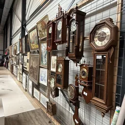 Uitgestalde collectie antieke wandklokken in houten kasten tegen een muur