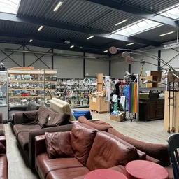 Winkelvloer met bruine leren zitmeubels, stellingen met diverse spullen, kledingrek en huisraad in kringloopwinkel