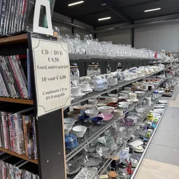 Lange tafel met uitgestald serviesgoed, glazen en huishoudartikelen in een kringloopwinkel