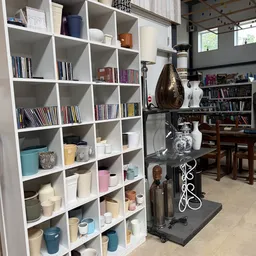 Winkelinterieur met witte kubuskasten vol boeken, decoratieartikelen en huishoudspullen, op de achtergrond boekenkasten en ho