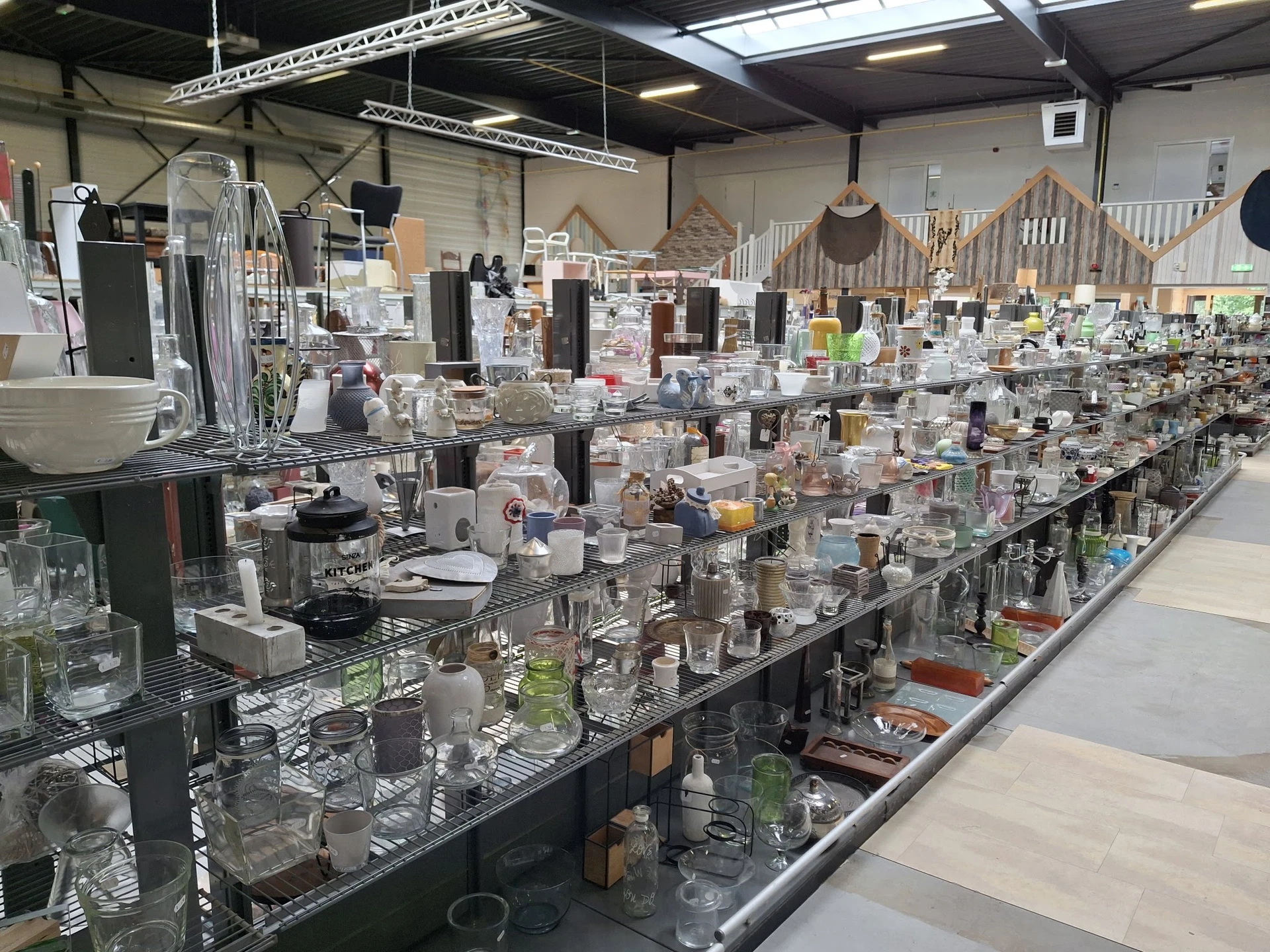 Lange toonbanken vol met glazen vazen, kaarsenhouders en huishoudelijke accessoires in verschillende maten en kleuren