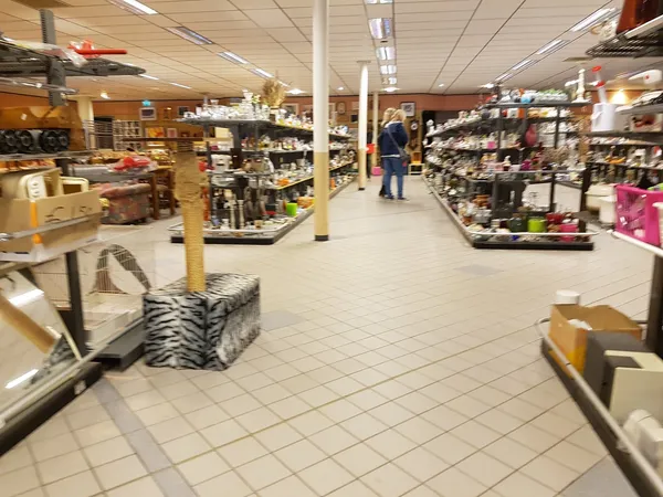Winkelvloer van kringloopwinkel met stellingen vol spullen, toonbanken en enkele bezoekers
