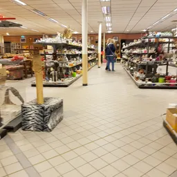 Winkelvloer van kringloopwinkel met stellingen vol spullen, zuilen, verlichting en enkele klanten