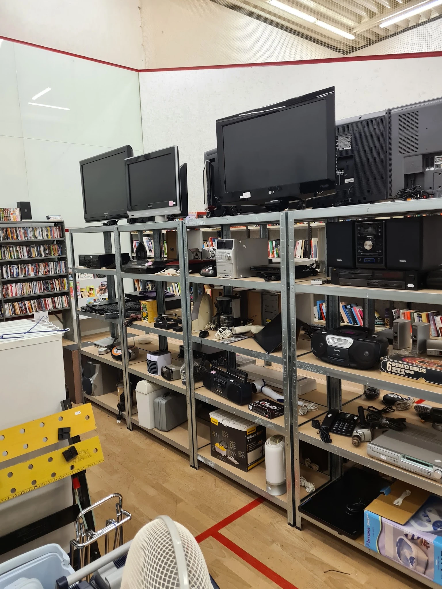 Metalen stellingen met elektronica, boeken en diverse tweedehands items in een kringloopwinkel