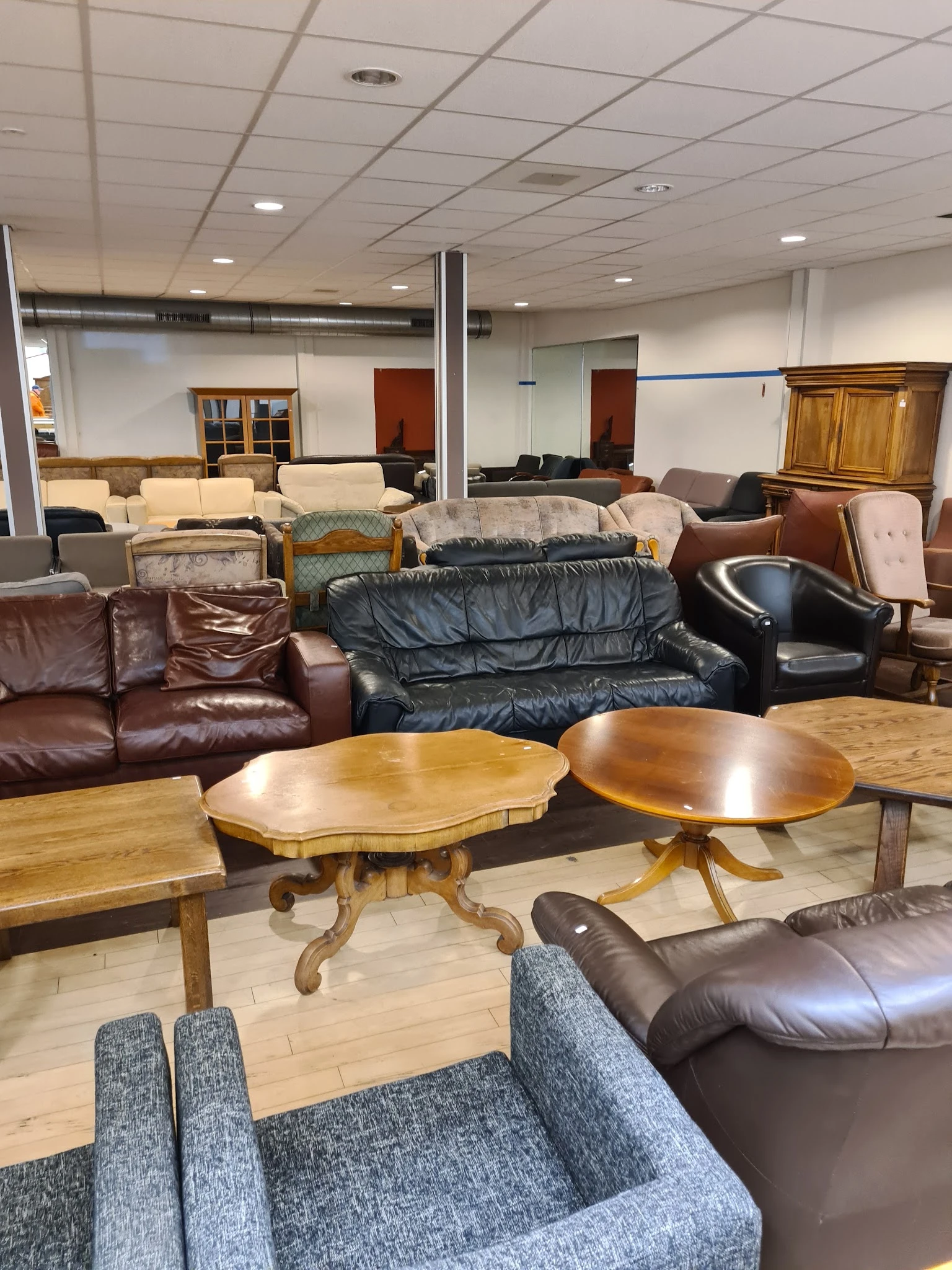 Uitgestalde meubels in een kringloopwinkel: diverse zitmeubels, houten tafels en kasten