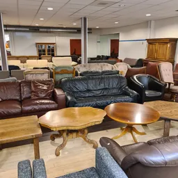 Uitgestalde meubels in een kringloopwinkel: diverse zitmeubels, houten tafels en kasten