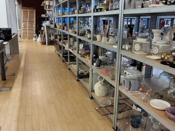 Lange winkelgang met metalen stellingen vol huishoudelijke artikelen en keukenspullen