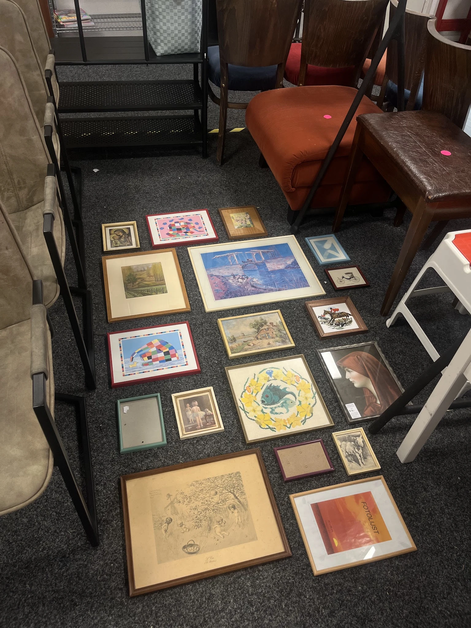 Diverse ingelijste prints, schilderijen en kunstwerken uitgestald op donkere vloer in de winkel