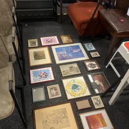 Diverse ingelijste prints, schilderijen en kunstwerken uitgestald op donkere vloer in de winkel