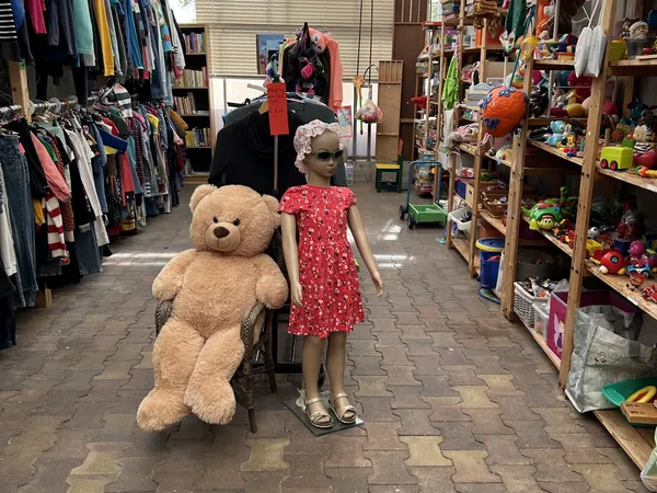 Winkelvloer met mannequin in rode jurk en grote teddybeer, omringd door kledingrekken en speelgoedrekken
