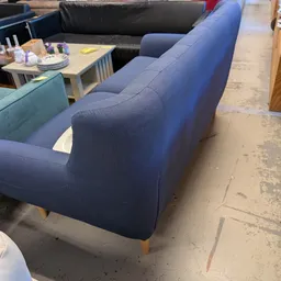 Blauwe tweedehands fauteuil met houten poten op betonnen vloer in de winkel