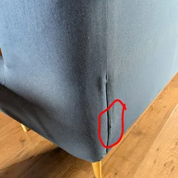 Close-up van een grijze stoffen meubelstuk met een naad, op houten vloer