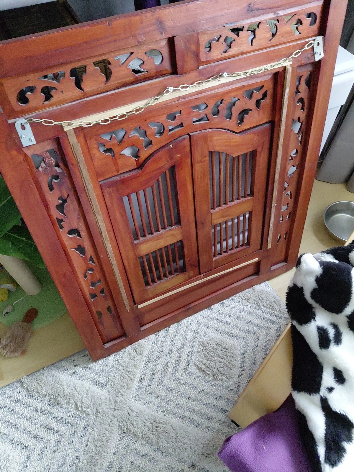 Rood houten kastje met decoratief snijwerk en roosters, staande op grijze ondergrond