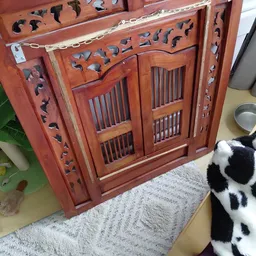 Rood houten kastje met decoratief snijwerk en roosters, staande op grijze ondergrond