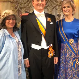 Drie personen in formele kleding met onderscheidingen poseren voor een foto