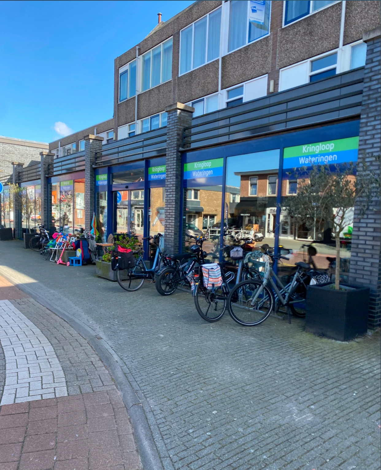 Winkelgevel met blauwe raampartijen en groene letters, fietsen geparkeerd voor de ingang