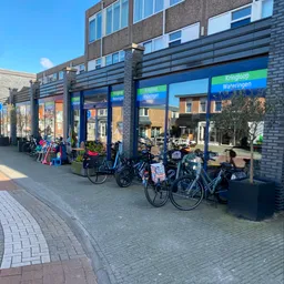 Winkelgevel met blauwe raampartijen en groene letters, fietsen geparkeerd voor de ingang