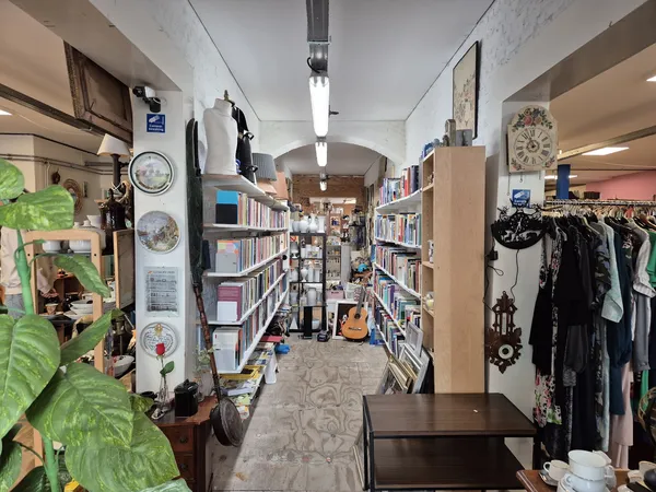 Winkelvloer van kringloopwinkel met boekenkasten, kledingrekken en diverse spullen langs de muren