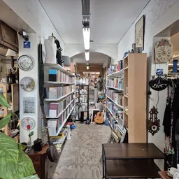 Winkelvloer van kringloopwinkel met boekenkasten, kledingrekken en diverse spullen langs de muren