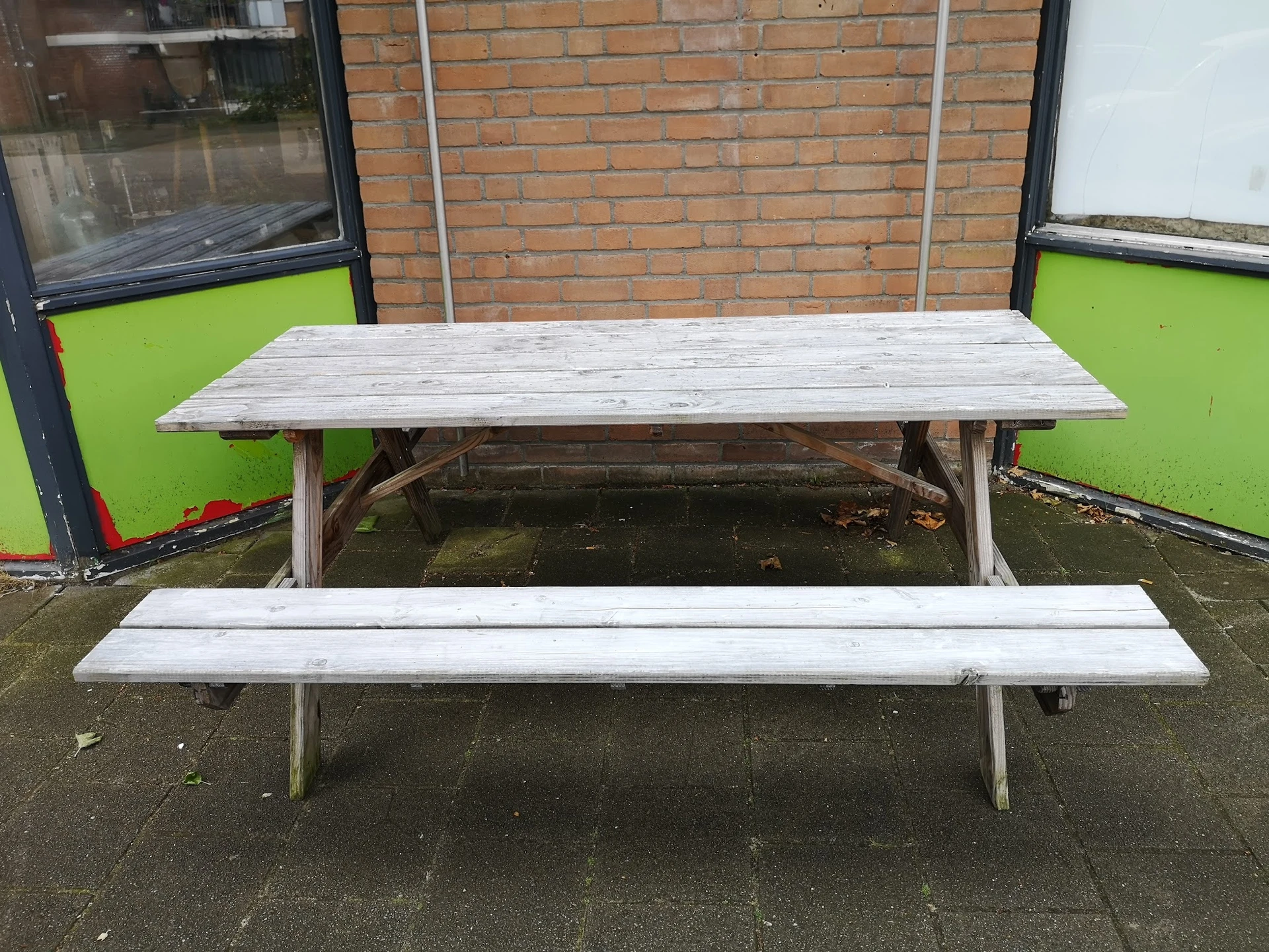 Picknickset met houten tafel en twee banken op een terras tegen een grijsgroene wand