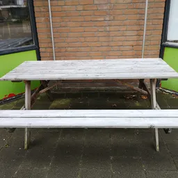 Picknickset met houten tafel en twee banken op een terras tegen een grijsgroene wand