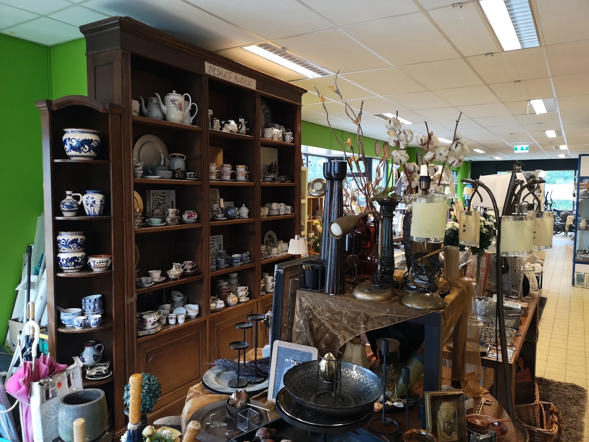 Winkelinterieur met houten vitrinekast vol servies en decoratieve items, daarnaast displays met verschillende gebruiksvoorwer