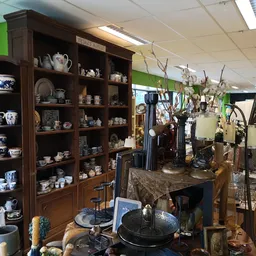 Winkelinterieur met houten vitrinekast vol servies en decoratieve items, daarnaast displays met verschillende gebruiksvoorwer