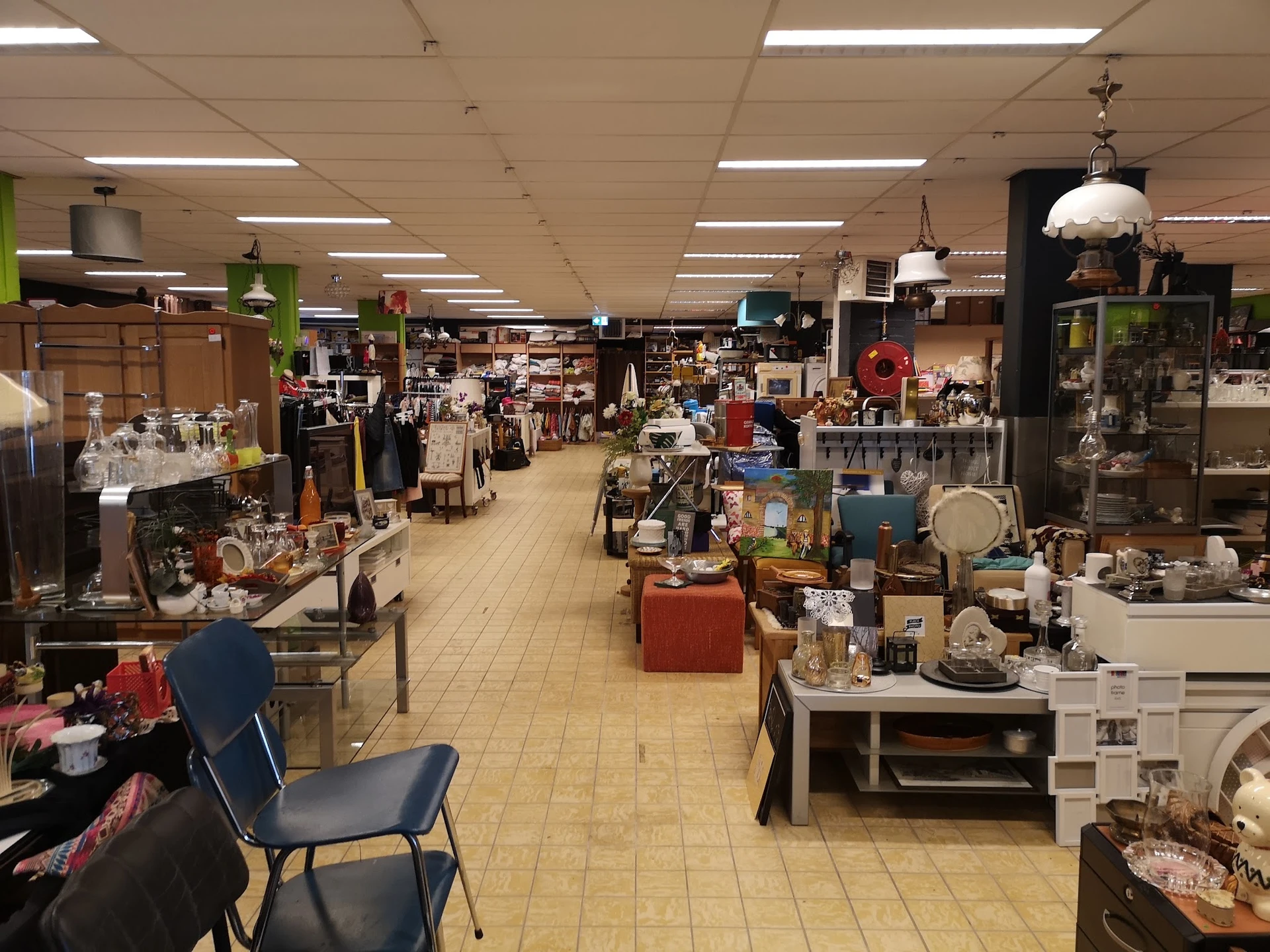 Ruime winkelvloer van kringloopwinkel met diverse stellingen, meubels en huishoudelijke artikelen uitgestald
