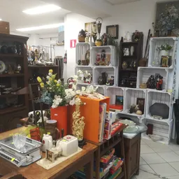Winkelvloer met houten tafel, bloemen in oranje vazen, boeken en diverse decoratieve artikelen, stellingen met verzamelobject