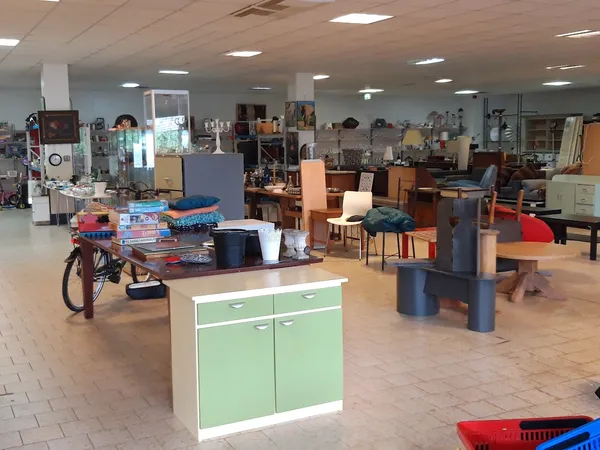 Ruim winkelinterieur met diverse meubels, een groene kast, fiets en spullen verspreid over de vloer