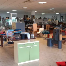 Ruim winkelinterieur met diverse meubels, een groene kast, fiets en spullen verspreid over de vloer