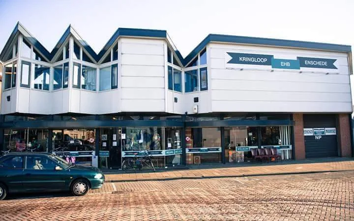 Witte en blauwe gevel van kringloopwinkel aan straat met etalage en ingang op begane grond