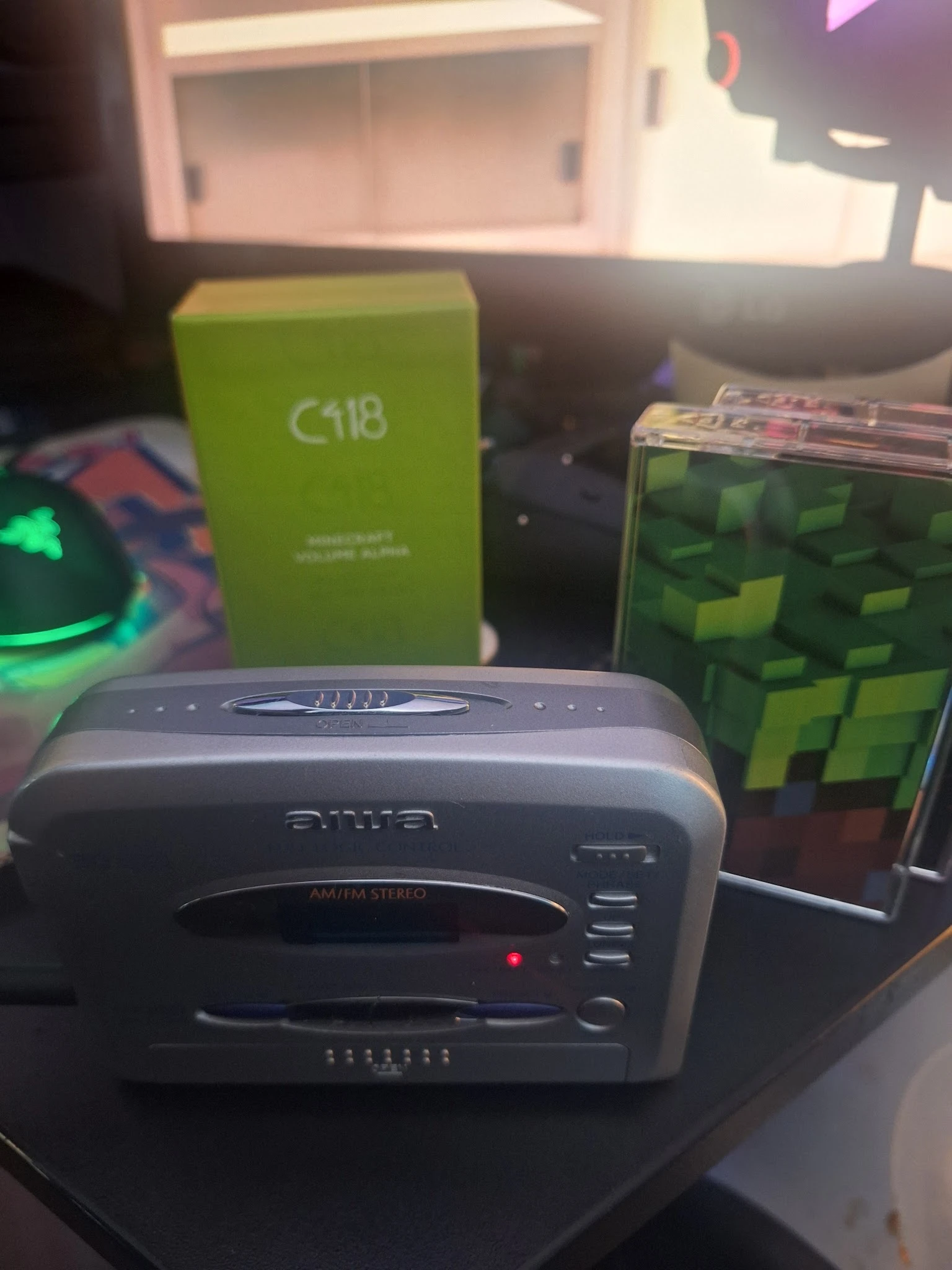 Diverse elektronica en gadgets op een tafel, waaronder een grijs apparaat, groene verpakkingen en een Minecraft-kubus