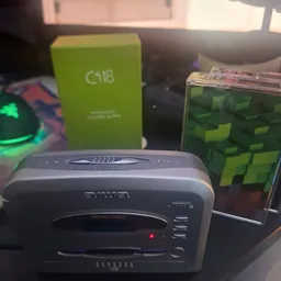 Diverse elektronica en gadgets op een tafel, waaronder een grijs apparaat, groene verpakkingen en een Minecraft-kubus