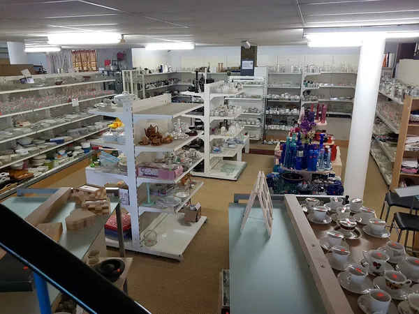 Overzicht van de kringloopwinkel met vitrines, stellingen en verschillende afdelingen met huishoudelijke artikelen en decorat